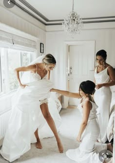 two bridesmaids helping the bride put on her wedding dress