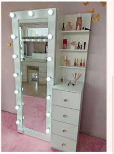 a white dresser sitting next to a mirror with lights on it's sides and drawers