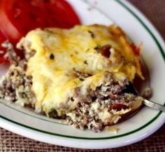 a white plate topped with meat and cheese covered in sauce next to a slice of tomato