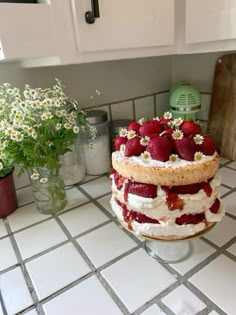 a cake sitting on top of a kitchen counter covered in strawberries and whipped cream