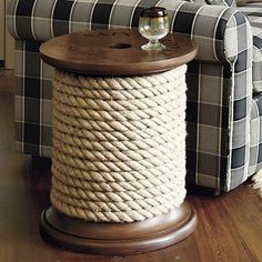 a rope covered end table next to a plaid couch with a wine glass on it