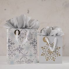 two gift bags with white paper and gold foil snowflakes are sitting on a table