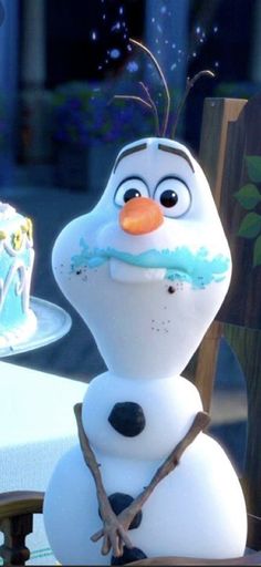 there is a frosted snowman with an orange nose and blue eyes next to a piece of cake