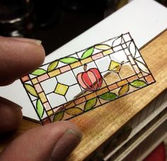 a hand holding a stained glass piece in front of a wooden box with an apple on it