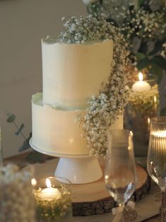 a white wedding cake sitting on top of a table next to wine glasses and candles