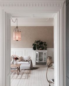 an open door leading to a living room with white furniture and plants on the wall