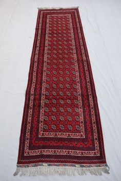 a red and black rug laying on top of a white bed cover with tassels