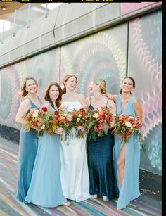 a group of women standing next to each other holding bouquets in front of a wall