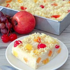 a piece of cake on a white plate next to a pan of fruit and a fork