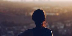 a woman standing in front of a cityscape with the sun shining through her hair