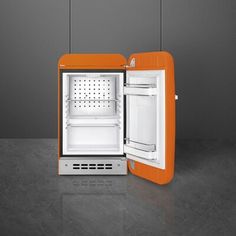 an orange refrigerator with its door open on a gray floored surface and two lights hanging from the ceiling