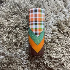 an orange, green and black plaid pattern is on the side of a cup that has been placed on a carpet