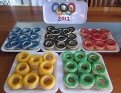 four trays filled with different colored doughnuts on top of a wooden table