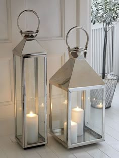 two white lanterns sitting on top of a floor next to each other with lit candles in them