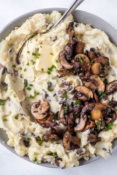 mashed potatoes with mushrooms and parsley in a gray bowl on a white surface