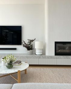 a living room with white furniture and a flat screen tv mounted on the wall above a fireplace