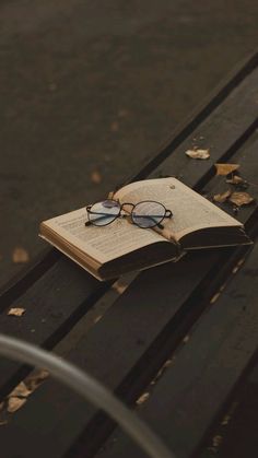 an open book with glasses resting on a park bench