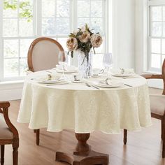 a dining room table set for four with flowers in vase and plates on the table