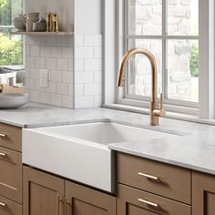 a white kitchen sink sitting under a window next to a counter top with gold faucets