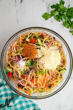 a glass bowl filled with pasta, vegetables and seasoning on top of a table