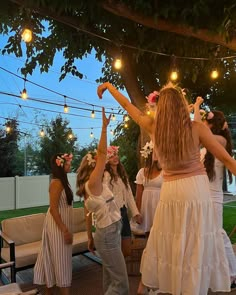 a group of women standing around each other in front of a tree with string lights