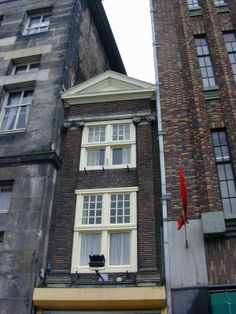 a tall brick building next to two smaller buildings with windows on each side and an orange flag hanging from the roof