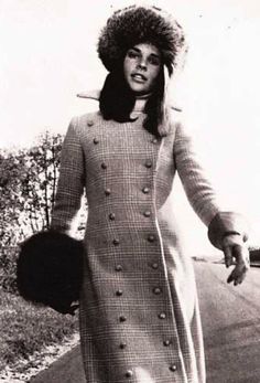 an old photo of a woman walking down the street wearing a coat and fur hat