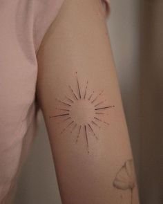 a woman's arm with a small sunburst tattoo on her left arm