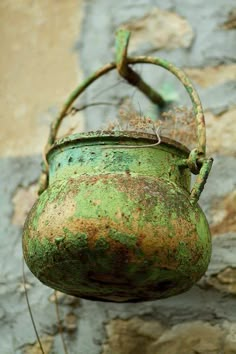 an old rusty green pot hanging from a brick wall with weeds growing out of it