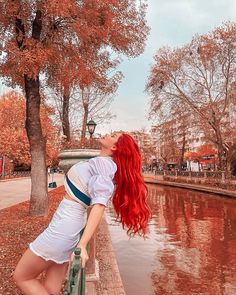 a woman with long red hair leaning on a wall next to a body of water