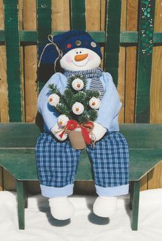 a snowman sitting on a chair holding a potted tree and wearing blue plaid pants