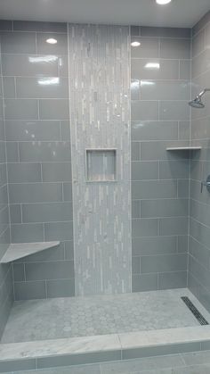 a walk in shower sitting next to a tiled wall and floor covered in gray tiles