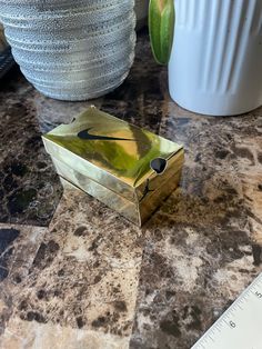 a gold box sitting on top of a counter next to a vase and measuring tape