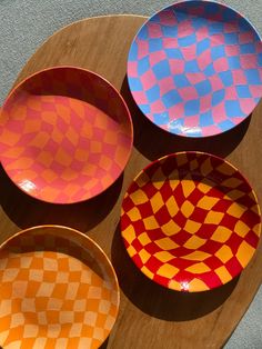 four different colored bowls sitting on top of a wooden table next to an orange and blue checkerboard pattern