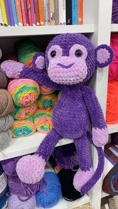 a purple monkey stuffed animal sitting on top of a book shelf filled with balls of yarn