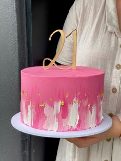 a woman holding a pink and gold cake with the number twenty one on it's side