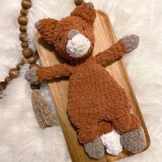 a brown teddy bear laying on top of a wooden board next to a beaded necklace