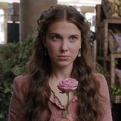 a woman with long hair holding a rose in her hand and looking at the camera