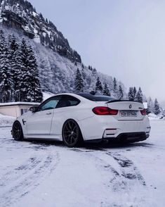 a white car parked in the middle of a snow covered road next to a mountain