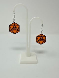 a pair of earrings with an orange and black design on them, hanging from a white stand