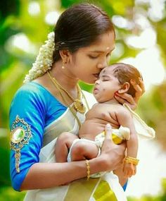 a woman holding a baby in her arms and kissing it's face with both hands