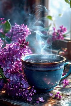 a blue cup with steam rising out of it next to purple lilacs on a wooden table