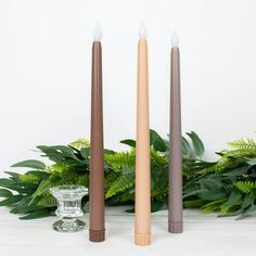 three candles sitting next to each other on top of a white table with greenery