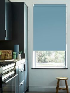 a kitchen with blue roller shades in the window, and a stool next to it