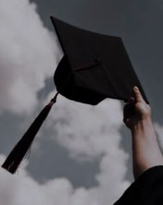 a person holding up a graduation cap in the air with clouds behind them and blue sky