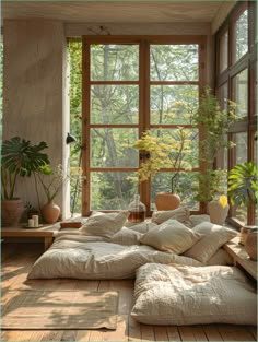 a large bed sitting under a window next to a plant filled room with lots of windows