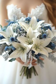 a bridal bouquet with white lilies and blue berries is held by a bride