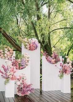 three white boxes with pink and purple flowers in them sitting on a wooden floor next to a tree