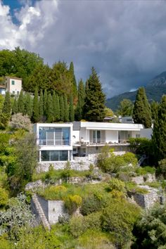 a large white house sitting on top of a lush green hillside next to trees and bushes