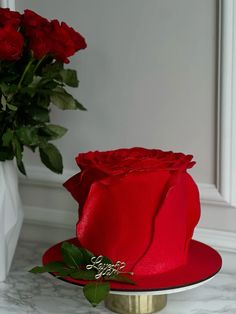 a red hat with a rose on it sitting next to a vase filled with flowers